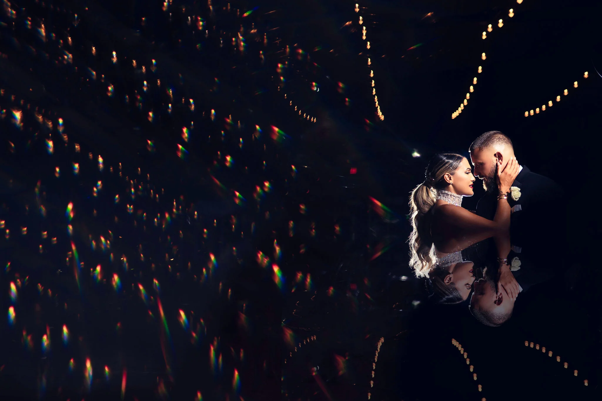 Bride and groom embracing closely in a dramatic lighting setting with reflections and prism flare
