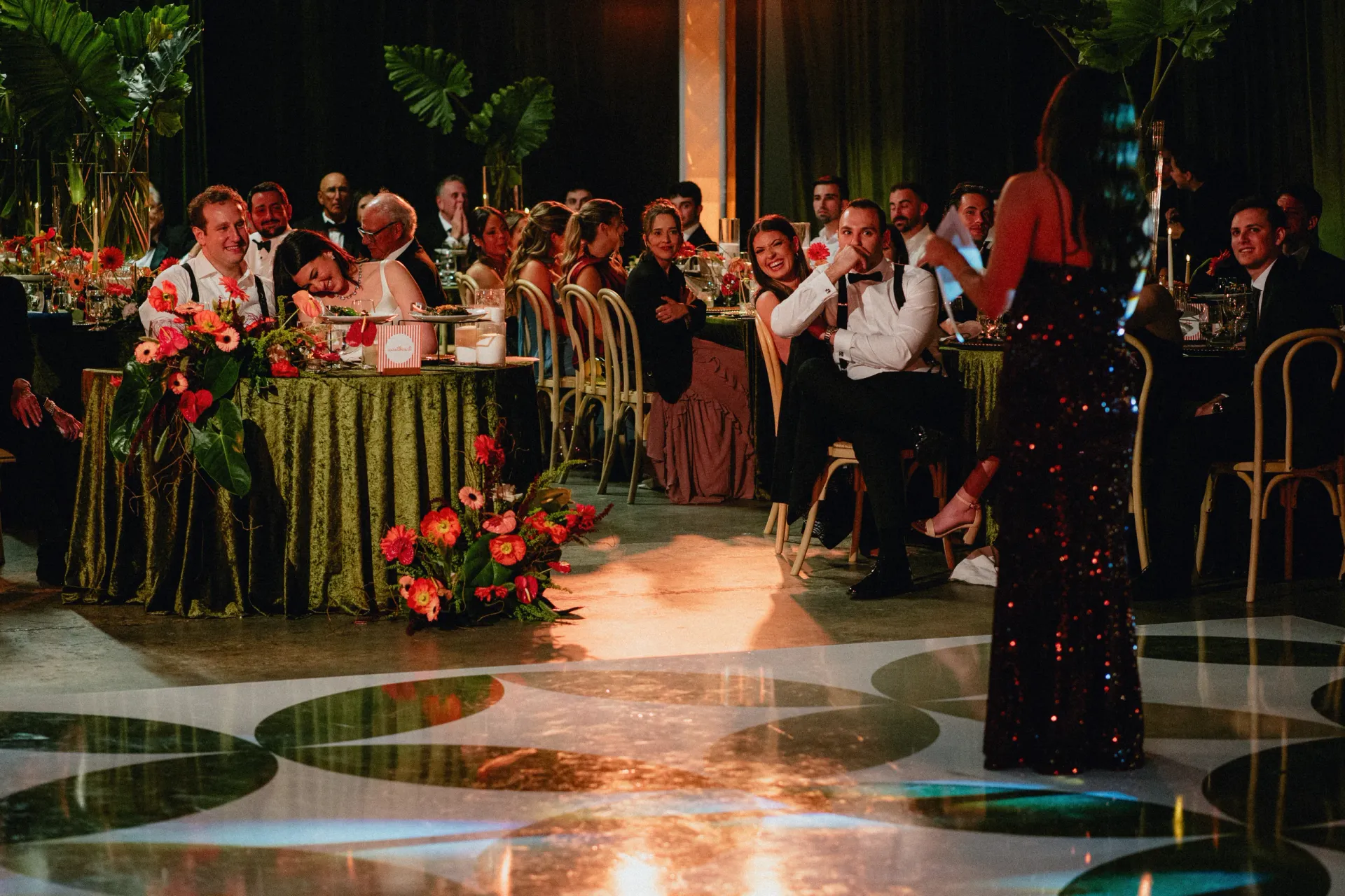 Bride and groom smiling at their sweetheart table during toasts surrounded by guests