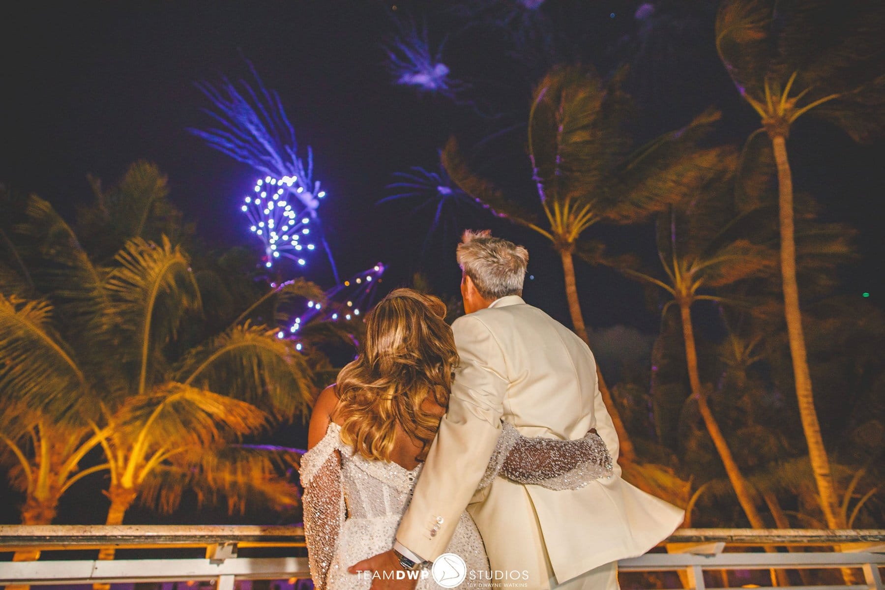 A couple beneath fireworks and palm trees at the close of the night