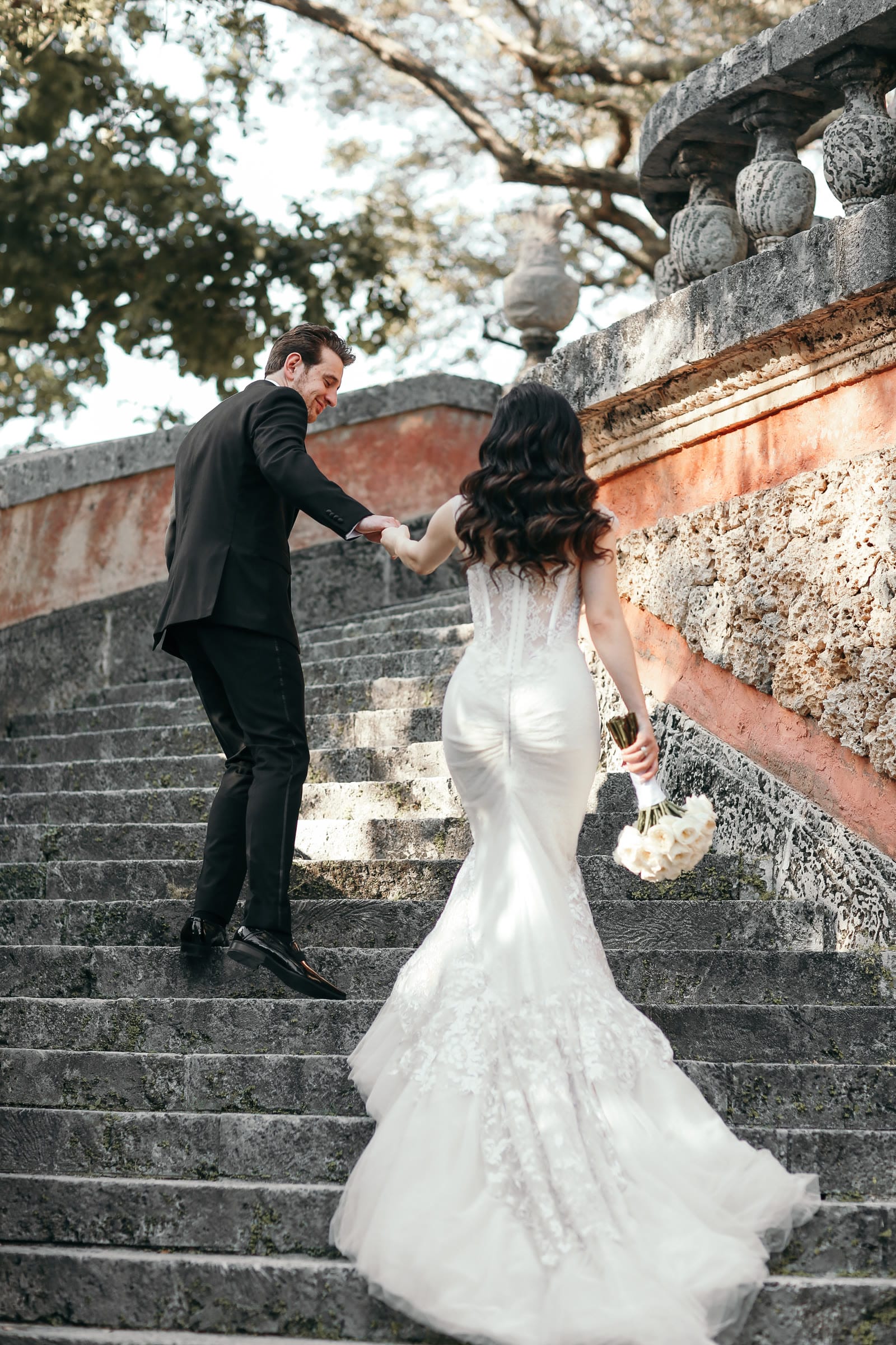 A newlywed couple walking together up the stone steps at Vizcaya
